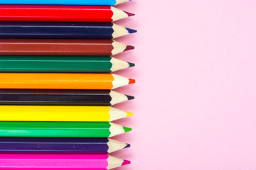 Multicolored pencils on pink paper background