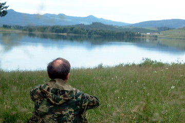 The man is sitting on the shore of the lake.