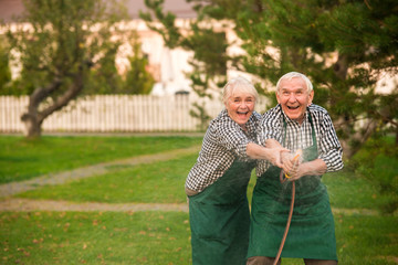 Old couple having fun. Happy people with garden hose.