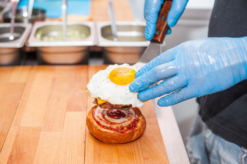 Chief cook preparing fresh burger in the kitchen.Burger restaurant menu cooking process. The cook puts frided egg with cutlet on the bun. Fast food cafe cuisine. Selective focus. close up.