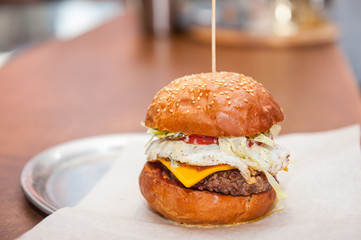 Fresh Tasty Beef Burger with lettuce, tomato, bacon, cheese and fried egg on a paper tray ready be take away on the bar counter. Selective focus, close up. Fast food cafe cuisine. Space for text.