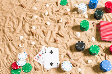 Gambling on vacation concept - white sand with seashells , colored poker chips and cards. Top view