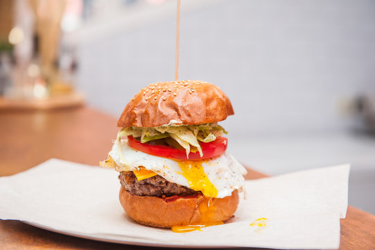 Fresh Tasty Beef Burger with lettuce, tomato, bacon, cheese and fried egg on a paper tray ready be take away on the bar counter. Selective focus, close up. Fast food cafe cuisine. Space for text.