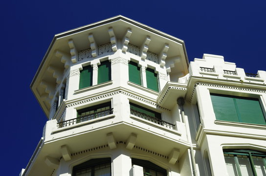 edificio blanco cl&aacute;sico con persianas y ventanas verdes