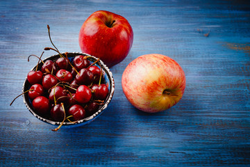 Apples and a bowl with a cherry on a blue table