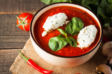 Chili tomato soup with sour cream sauce, cottage cheese, basil and red hot peppers on wooden background. Healthy, vegan and dieting lunch and dinner concept.