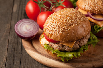 Close-up photo of home made hamburger with beer made of beef, onion, tomato, lettuce, cheese and spices. Fresh burger closeup on wooden rustic table with potato fries and chips.