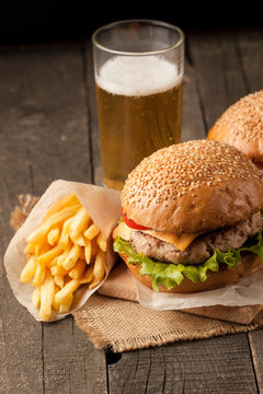 Close-up photo of home made hamburger with beer made of beef, onion, tomato, lettuce, cheese and spices. Fresh burger closeup on wooden rustic table with potato fries and chips.