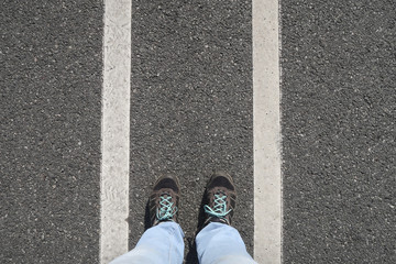 Person standing between two white stripes on concrete seen high angle just the feet between the lines