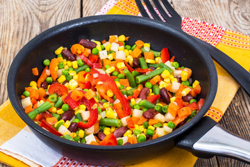 Cooked mixed vegetables in frying pan on wooden table