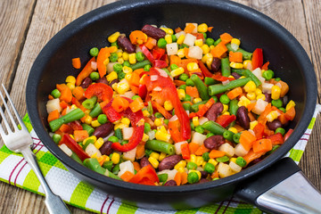 Cooked mixed vegetables in frying pan on wooden table