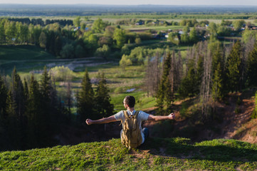 Naklejka na ściany i meble Young man tourist with backpack standing on the edge of beautiful canyon and victoriously raised hands. Male hiker reaching up top of mountain and outstretching arms up. Rear back view.