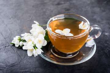 Cup of tea and jasmine flowers on a dark concrete  background