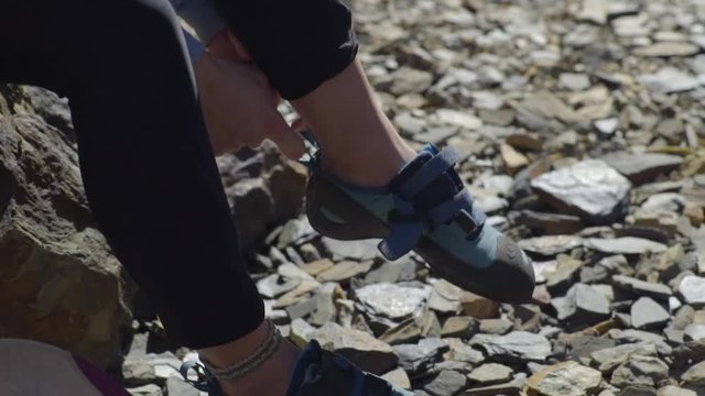 Closeup Of Young Woman Putting On Her Rock Climbing Shoes, She Secures Velcro Straps, Reaches For Her Climbing Harness