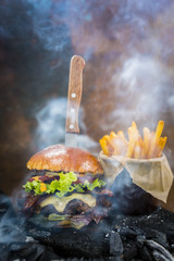 Tasty smoked and grilled beef burger with lettuce, cheese and bacon served with french fries on...