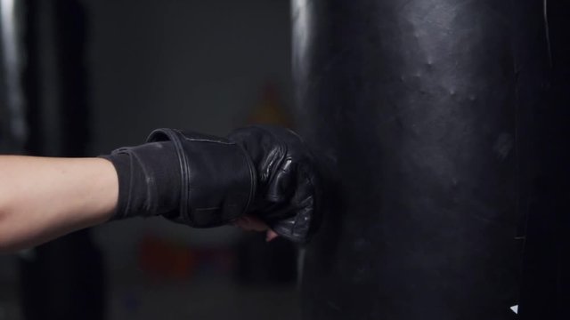 Closeup view of a woman's hand in boxing gloves punching a bag in a boxing club. Slowmotion shot