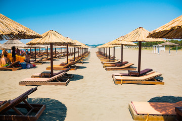 Luxury sand beach with wooden chaise-longue chairs and umbrellas on the beach