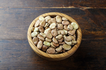 Dried broad beans in a wooden bowl on a wooden background. Top view, space for text