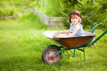 Blonde toddler girl sitting in a wheelbarrow in domestic garden