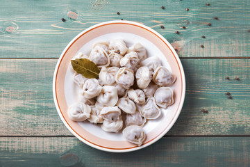 Homemade Meat Dumplings - russian pelmeni with laurel leaf on plate and green wooden background with pepper. Top view