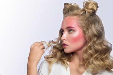Beautiful blonde woman face with pink makeup. Glamour fashion model portrait with colorful pigment on the face, glossy skin, bright make-up, bun hairstyle. White backdrop