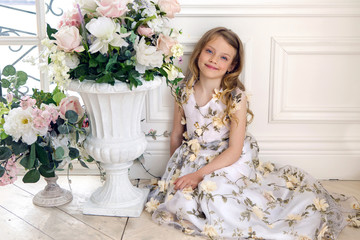 girl in floral dress sitting on the floor next to a white stone vase flowers wall
