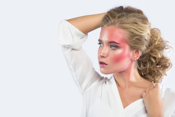 Beautiful blonde woman face with pink makeup. Glamour fashion model portrait with colorful pigment on the face, glossy skin, bright make-up. White backdrop