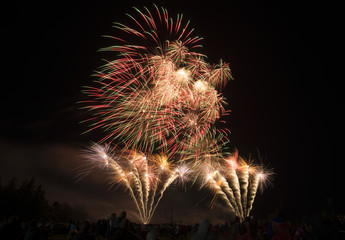 Many beautiful bursting forworks over park where people sit