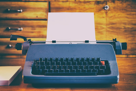 Old blue retro typewriter with a clean sheet of paper in a antique wooden room. 