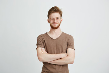 Portrait of happy cheerful young man with beard smiling looking at camera with crossed arms over...