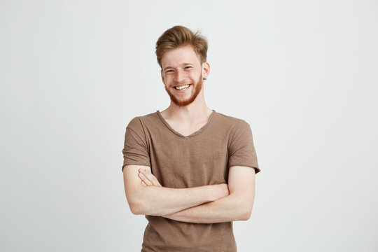 Portrait of happy cheerful young man with beard smiling looking at camera with crossed arms over white background.