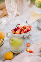 wedding, nutrition, decoration, food, nature concept - yellow and red cherries lying in gravy boat with floral print nearby crystal wine-glasses and apricotes
