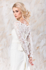 fashionable white gown, beautiful blonde model, bride hairstyle and makeup concept - young charming lady in wedding festive dress standing indoors on light background, pretty woman posing