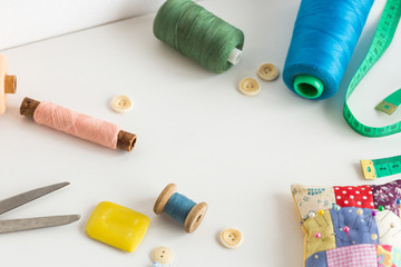 Fototapeta na wymiar sewing tools, patchwork, tailoring and fashion concept - closeup on white desk in studio, colorful thread spools, measuring meter, buttons, many worked scissors, pincushion, equipment for needlework.