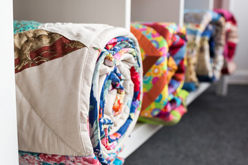 patchwork, sewing and fashion concept - bright finished quilts in the studio at white shelves with three storage compartments, the warehouse of finished products, side view, selective focus