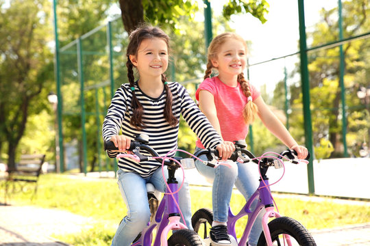 Cute girls riding bicycles in park on sunny day