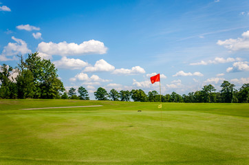 Golf course with beautiful green grass, bright blue skies and white puffy clouds.  Recreational...