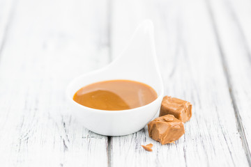 Portion of Caramel Sauce on wooden background (selective focus)
