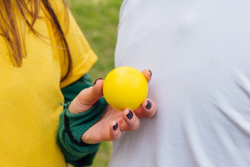 Colorful background of people in yellow and white tee shirt with a hand holding a yellow ball. Shallow DOF/ A beautiful woman hand holds a yellow sphere