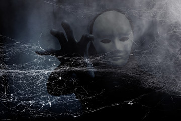 Mysterious woman in black wearing white mask hidden behind spider web,Scary background for book...