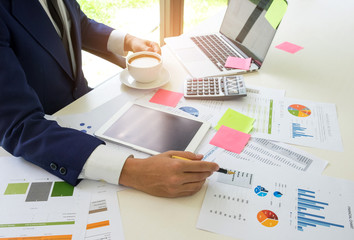Concept of a business man analyzes data online with the internet and eating coffee.Businessmen are analyzing graphs and on the desk with a laptop, tablet, calculator and eat coffee.