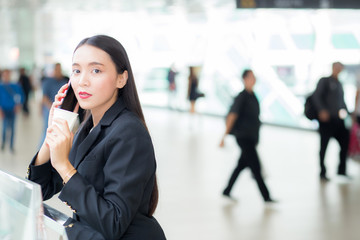 Asian businesswoman talking mobile phone and holding a coffee cup against urban scene, business concept.