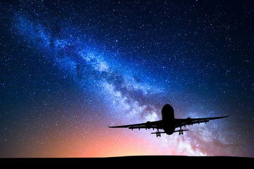 Milky Way and silhouette of a airplane. Landscape with passenger airplane is flying in the starry sky at night. Space background. Commercial airliner on the background of colorful Milky Way. Aircraft