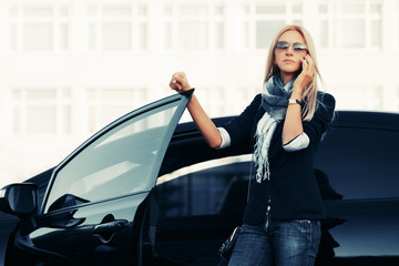 Fashion business woman in sunglasses talking on cell phone beside a her car