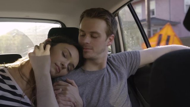 Woman Rests Her Head On Her Boyfriend's Shoulder, In Back Seat Of Car, He Kisses Her Head And Strokes Her Hair (Slow Motion)