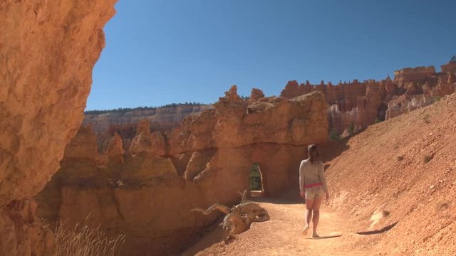 Happy female hiker walking along an empty path exploring stunning Bryce Canyon National Park in sunny Utah. Young woman tourist hiking a trail into Bryce Canyon, visiting national parks and landmarks