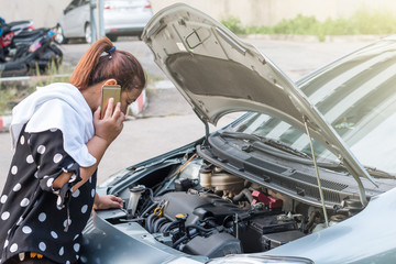 The woman talking on smartphone and looking to engine room of broken down car