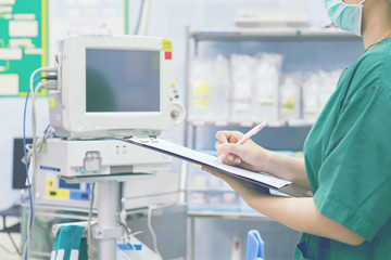female doctor with stethoscope on hospital corridor holding clipboard and writing prescription with an operating room at the background ,Healthcare and medical concept,selective focus