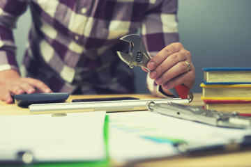 Hand 's engineer  holding tools with wrenches, pliers, screwdrivers, hammer and insulating adhesive tape on old wooden desk and calculate project with digital calculator,vintage color