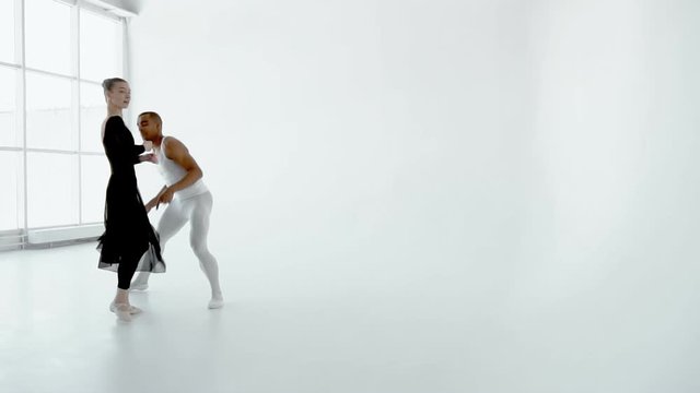 Young 20s attractive couple of dancers gracefully dancing in big white dance class, a guy holding a girl in his arms slow motion 120fps.